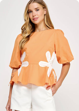 Woman wearing an orange blouse with white floral designs on cinched waist and puff sleeve