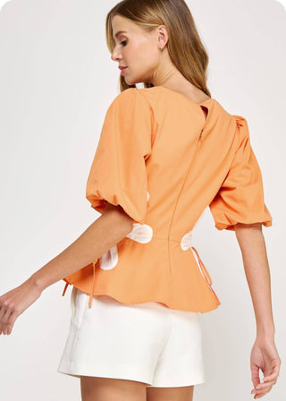 Woman wearing an orange blouse with puff sleeves showing back of blouse