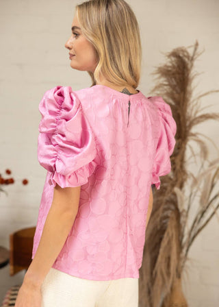 Woman wearing a pink blouse with puff sleeves in an indoor setting.