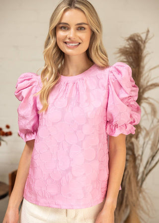 Woman wearing a pink blouse with puff sleeves against a neutral background