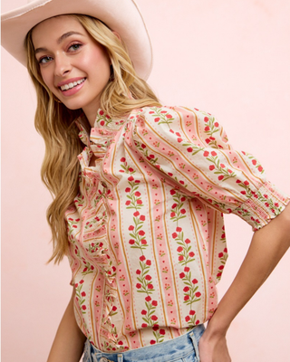 Pink floral ruffle puff sleeve blouse with high neckline paired with light wash denim jeans and a white cowboy hat.