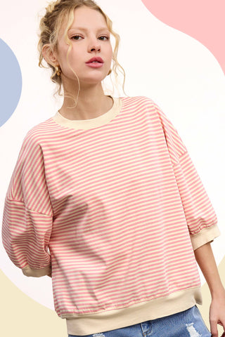 Woman wearing an oversized pink and cream striped knit pullover with drop shoulders and wide sleeves, styled with distressed denim for a casual boutique look.
