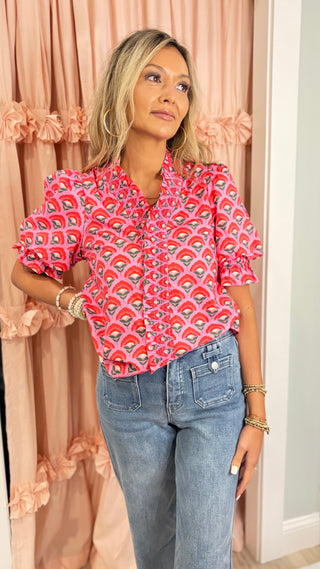 Woman wearing a bright pink floral ruffle blouse with puff sleeves styled with light wash high-waisted jeans for a chic boutique outfit.
