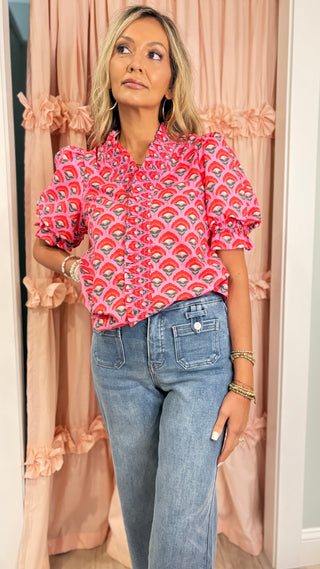Woman wearing a bright pink floral ruffle blouse with puff sleeves styled with light wash high-waisted jeans for a chic boutique outfit.