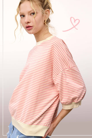 Woman wearing an oversized pink and cream striped knit pullover with drop shoulders and wide sleeves, styled with distressed denim for a casual boutique look.