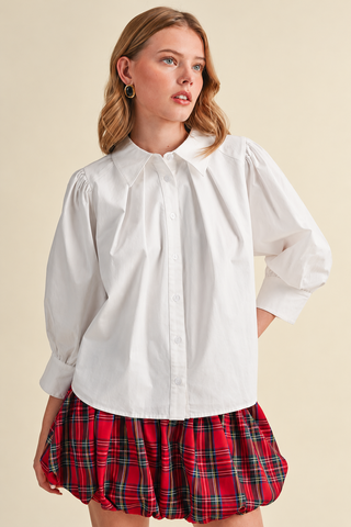 Model wearing a white button-down blouse with puff sleeves, pointed collar, and wide cuffs, paired with a red plaid bubble skirt.