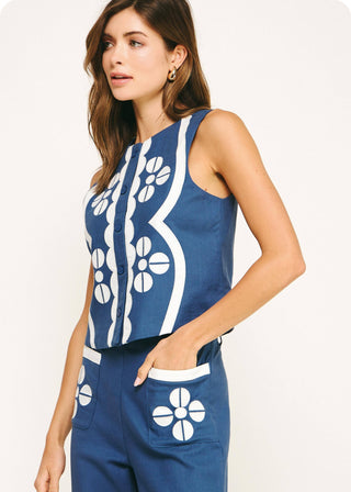 Woman wearing a blue sleeveless top and pants with white floral patterns on a white background