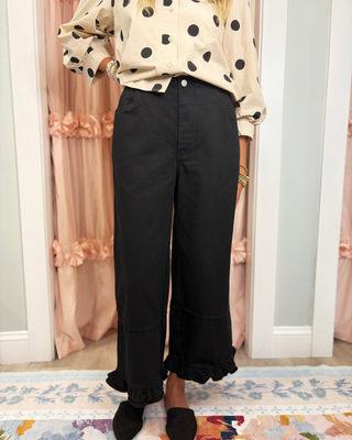 Women's black high-rise wide-leg cropped pants with a ruffle hem, functional pockets, and a relaxed fit, styled with casual sneakers for a chic boutique look.