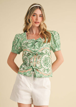 Woman wearing a square neck puff sleeve sage green medallion print blouse with front tie accents