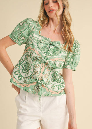 Woman wearing a sage green medallion print puff sleeve flowy blouse with front tie accents