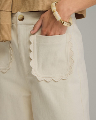 Women's ivory wide-leg pants with a high-rise waist and decorative scalloped front pockets, styled for a chic boutique outfit.