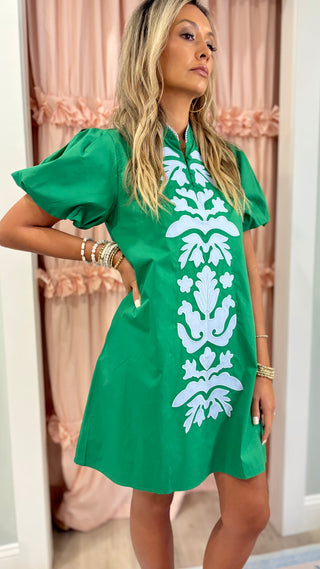 Woman wearing an emerald green embroidered shift dress with white appliqué detailing and puff sleeves, styled for a chic boutique fashion look.