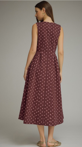 Back view of round neckline sleeveless crimson dress with pink polka dots a gathered waist forming waist with an A-line pleated midi skirt