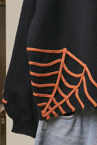 Black Halloween knit sweater with orange embroidered spiderweb designs and hanging spider detail, styled with distressed denim shorts.