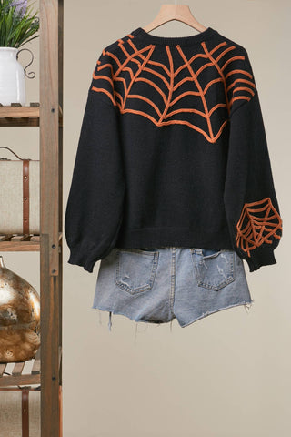 Black Halloween knit sweater with orange embroidered spiderweb designs and hanging spider detail, styled with distressed denim shorts.