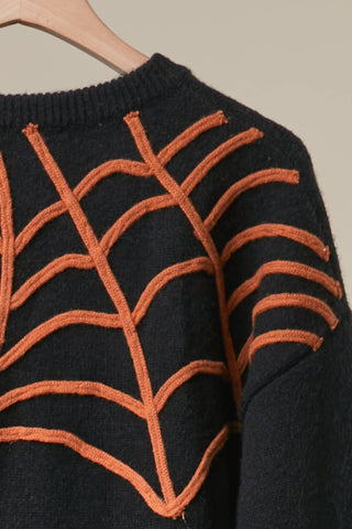 Black Halloween knit sweater with orange embroidered spiderweb designs and hanging spider detail, styled with distressed denim shorts.