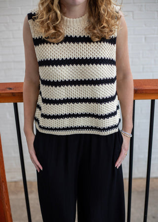 A woman wearing a sleeveless knit top with horizontal black and cream stripes, paired with black pants