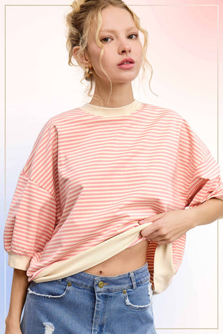 Woman wearing an oversized pink and cream striped knit pullover with drop shoulders and wide sleeves, styled with distressed denim for a casual boutique look.