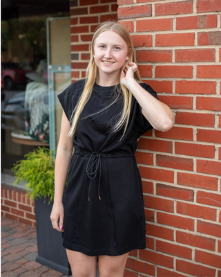 Model wearing a black drawstring shift mini dress with cap sleeves, side pockets, and a crew neckline.