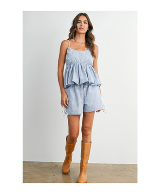 The Bluebell Peplum Top featuring a soft blue gingham print, adjustable spaghetti straps, a flattering peplum silhouette, and a statement bow tie back.