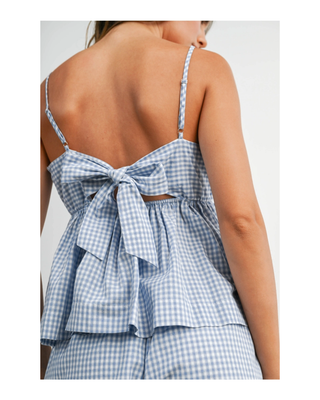 The Bluebell Peplum Top featuring a soft blue gingham print, adjustable spaghetti straps, a flattering peplum silhouette, and a statement bow tie back.