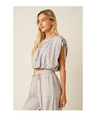 The Maren Bubble Top in light gray featuring textured fabric, adjustable shoulder ties, an elastic neckline, and a flattering bubble hem.
