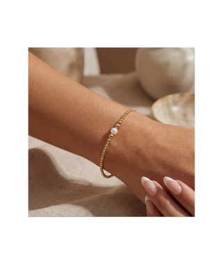 Gold beaded bracelet with single pearl accent worn on wrist, a delicate women’s jewelry accessory.