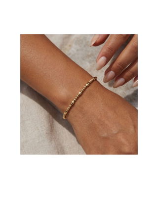 Delicate gold beaded bracelet with polished oval bead accents worn on a woman’s wrist.