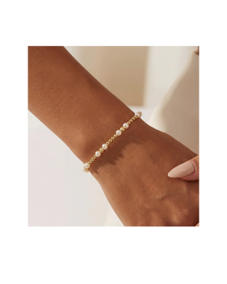 Delicate gold beaded bracelet featuring classic pearl accents worn on a woman’s wrist.