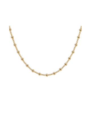 Delicate gold beaded necklace with alternating bead sizes worn as a short necklace for women.