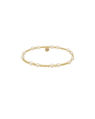 Delicate gold beaded bracelet featuring classic pearl accents worn on a woman’s wrist.