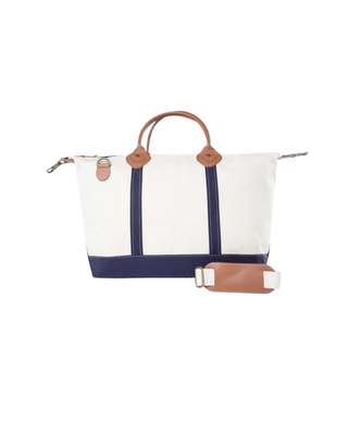Weekender travel bag featuring durable natural canvas, navy trim, genuine leather handles, removable shoulder strap, and a spacious zip-top interior.