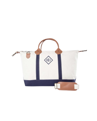 Weekender travel bag featuring durable natural canvas, navy trim, genuine leather handles, removable shoulder strap, and a spacious zip-top interior.