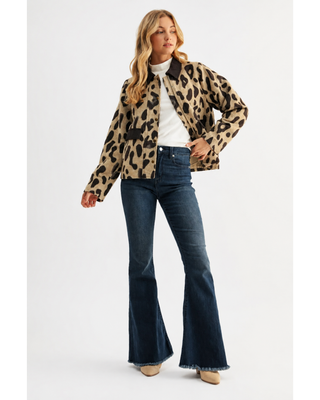 Woman wearing a taupe and dark brown leopard print zip-front jacket with a contrasting brown collar and pocket trim, styled with a white top and dark denim jeans.