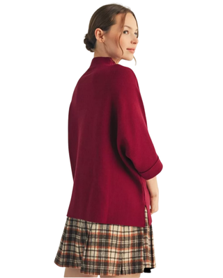 Women’s burgundy mock neck sweater top with elbow-length sleeves styled with a plaid pleated skirt.