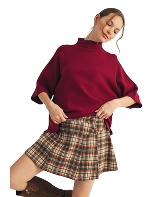 Women’s burgundy mock neck sweater top with elbow-length sleeves styled with a plaid pleated skirt.