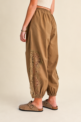 Women's camel balloon pants with floral lace inset detailing, elastic drawstring waistband, relaxed fit, and gathered ankle cuffs, styled with tan clogs.