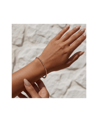 Close-up of a delicate metallic beaded bracelet worn on the wrist with a neutral stone background.