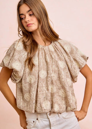 Woman wearing a beige lace bubble hem puff sleeve blouse against a pink background