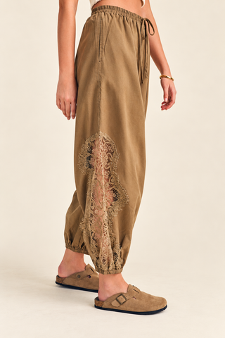 Women's camel balloon pants with floral lace inset detailing, elastic drawstring waistband, relaxed fit, and gathered ankle cuffs, styled with tan clogs.